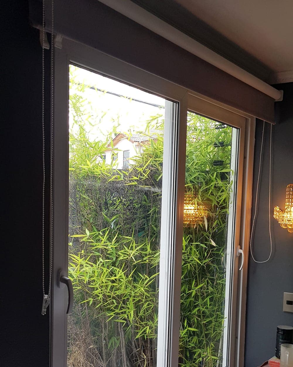 Ventana corredera de PVC blanco con vista a un jardín de bambú